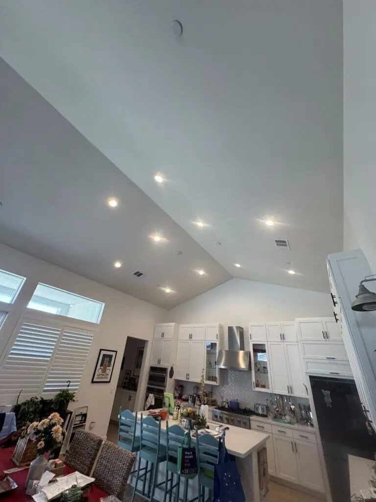 Recessed ceiling lights illuminate this modern kitchen with white cabinetry and stainless steel appl.