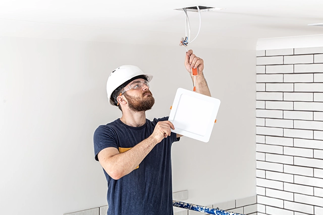 Electrician Installing Ceiling Light Fixture in a Modern White Room